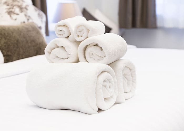 Frisch gewaschene, aufgerollte Handtücher auf Hotelbett – Wäscheservice von Glanz & Glorie Hotel Service für Hotels und Resorts
